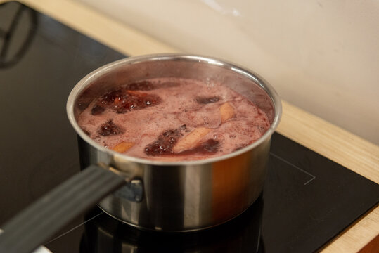 Fruit and berry compote boiling in stainless pot on stove for cooking and healthy beverage preparation background
