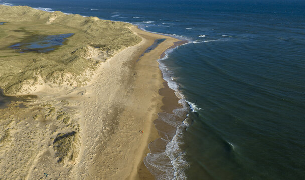 Aerial view of a vast sandy beach and rolling grassy dunes with a person walking along the shore, Peterhead, Scotland, United Kingdom.