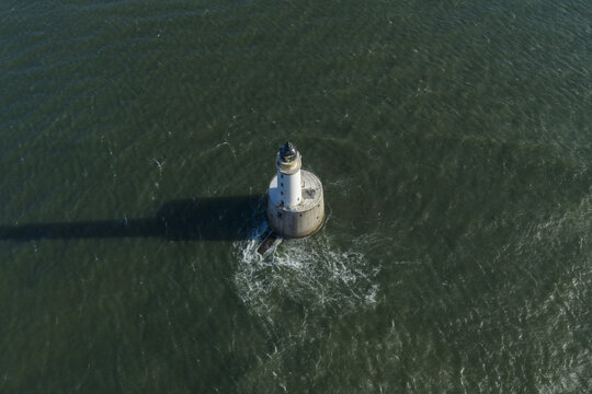 Aerial view of Rattray Head Lighthouse standing in the dark green sea with a long shadow and gentle ripples Peterhead, Scotland, United Kingdom.