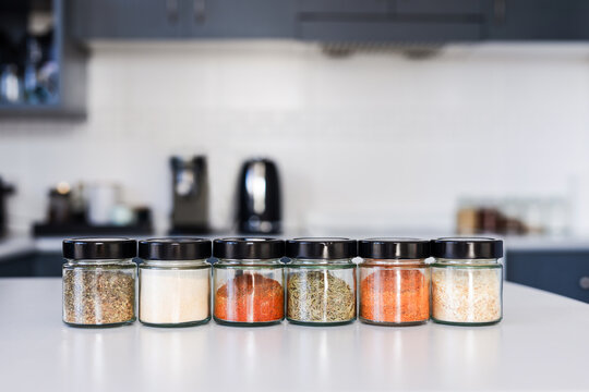 tidy spices and herbs in matching jars on kitchen countertop with soft kitchen bokeh background
