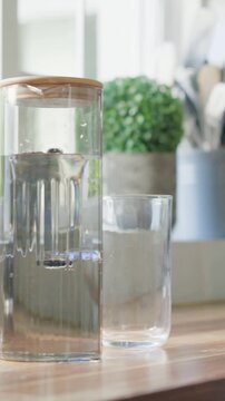 Vertical video: Bubbling infuser carafe releasing beads at kitchen counter from sun heat, tumbler