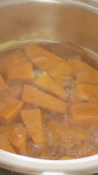 Vertical video: Boiling orange chunks bobbing, tumbling, settling in steel pot on stove for cooking