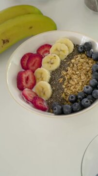 Vertical video: Panning handheld camera revealing breakfast bowl on white countertop with jars