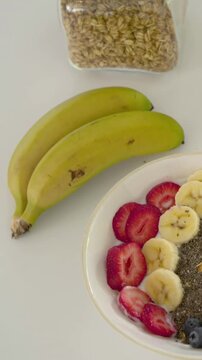 Vertical video: Starting pan, camera revealing pair of bananas on white tabletop, jar of oats seen