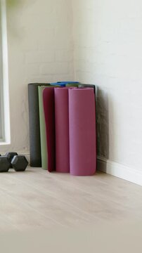 Vertical video: Recording rolled mats standing in home corner with hex weights on wooden floor