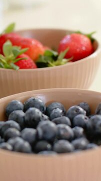 Vertical video: Panning shot showing blueberry and strawberry bowls on kitchen top with amber jar