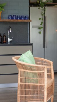 Vertical video: Camera shifting left up showing rattan chair with mint cushion in kitchen, fridge