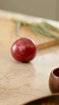 Vertical video: Pulling back camera revealing red onion on counter to reveal board, scallion, bowls