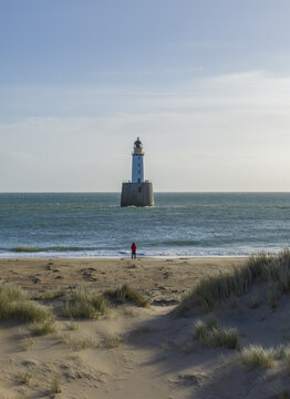Aerial view of Rattray Head Lighthouse rising from the sea with a person standing on the sandy beach and dunes in Peterhead, Scotland, United Kingdom.