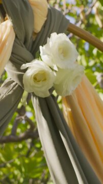 Vertical video: Tilting shot framing tied drapes and white roses on pole in garden, breeze stirring