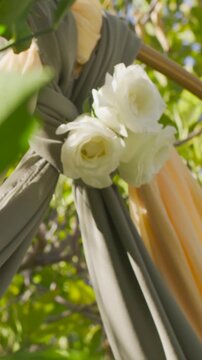 Vertical video: Camera pulling back revealing two knotted fabric panels at garden with white roses