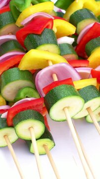 Vertical video: Shifting camera revealing pile of skewers with zucchini and peppers on white plate