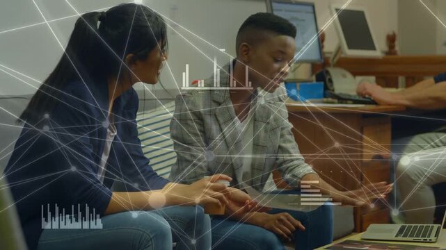 Two women leaning on sofa, pointing and reaching toward laptop, matching pamphlet with tech charts