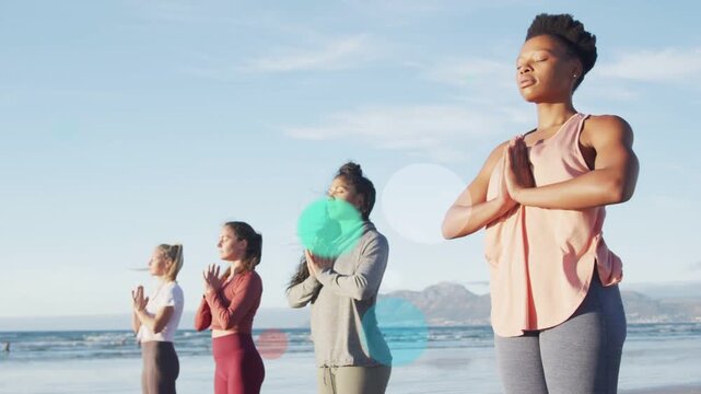 Rightmost woman holding prayer pose on sand midway soft discs rising, guiding meditation