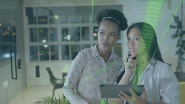 Two women analysts tapping tablet and manipulating projected green charts for business decisions