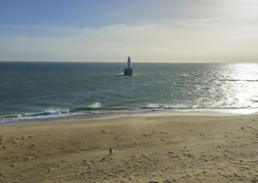 Aerial view of Rattray Head Lighthouse standing in the North Sea with a person on the sandy beach under a bright sky Peterhead, Scotland, United Kingdom.
