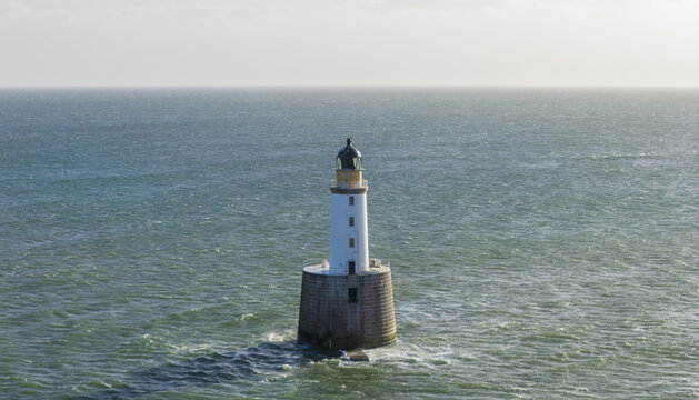 Aerial view of Rattray Head Lighthouse standing in the North Sea with gentle waves and a clear horizon near Peterhead, Scotland, United Kingdom.