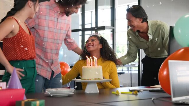 Man carrying lit cake entering while team clapping, surprising seated teammate for office birthday