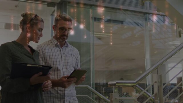 Staff pair ascending stairs, man tapping tablet causing falling light, checking binder for business