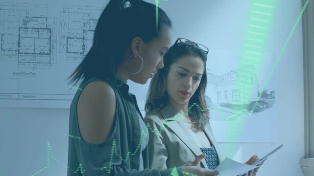 Two women reviewing plans right tapping tablet causing finance charts overlaying papers for audit