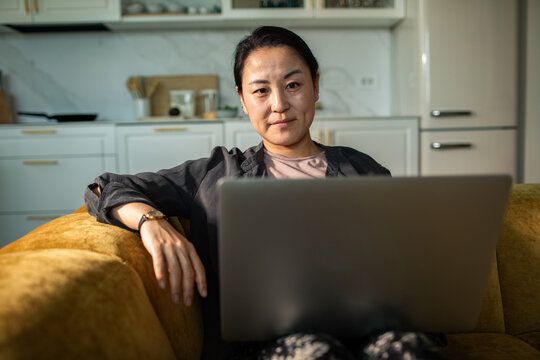 Woman working on laptop on sofa in home kitchen