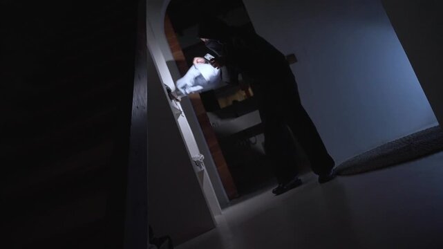 Burglar with flashlight breaking into house at night
