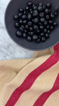 blueberries cascading onto a clean black plate. The scene captures the dynamic, fresh motion with some berries in mid-air and others piling up, highlighting the deep blue, natural bloom-coated texture