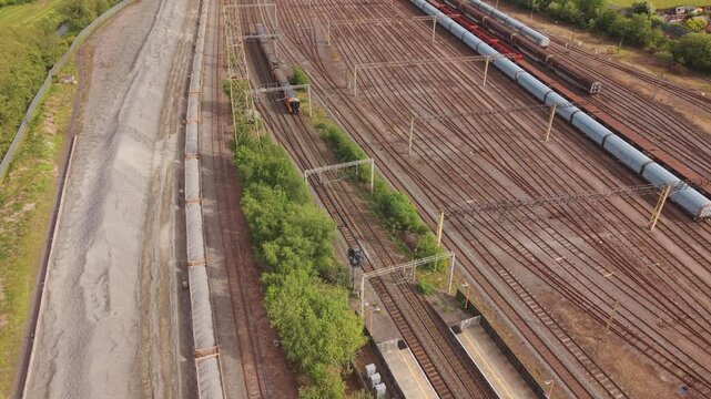 Cinematic drone footage flying above a large railway yard in Birmingham UK with multiple train tracks, freight wagons, industrial infrastructure and urban surroundings. Aerial view of British rail tra