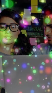 Vertical video: Man studying laptop, woman joining, starting design review, bokeh over sticky notes