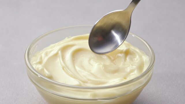 Close up of scooping creamy mayonnaise with a spoon from a glass bowl