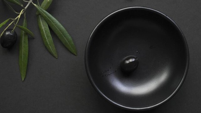Black_olives_filling_empty_black_bowl_on_black_background