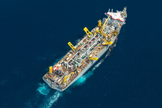 Aerial view of a large dredger vessel with yellow cranes navigating the deep blue ocean waters near Vashafaru, Haa Alif Atoll, Maldives.