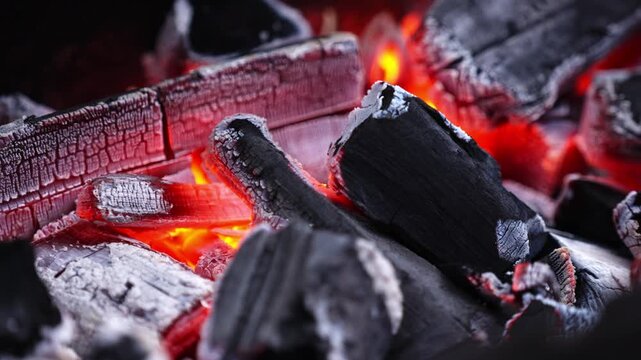Burning charcoal pieces glowing with intense heat and ash forming in close up fire scene