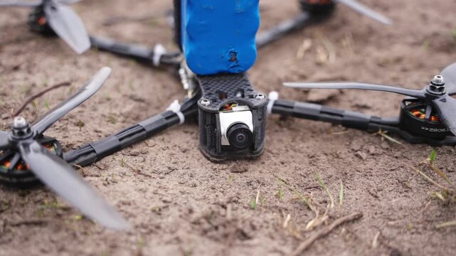 Detailed close up of FPV drone components on dirt ground showing camera and frame setup