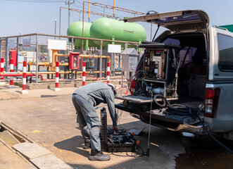 Naklejka premium A field technician in industrial workwear unloading environmental air quality monitoring equipment and mobile sampling instruments from the back of a pickup truck at an industrial site.