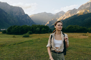 Obraz premium Woman with backpack exploring a landscape valley and mountains, outdoors in nature, hiking and adventure lifestyle in a meadow scene, smiling and confident.