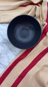 A dark, mate ceramic dish is set down on a marble surface table.