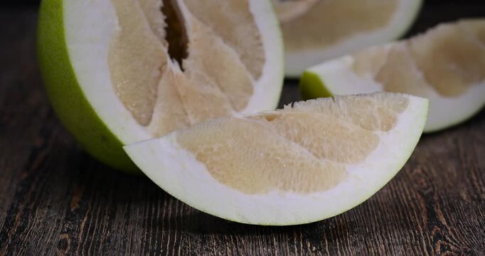 large citrus fruit cut into several pieces with juicy sweet flesh, large citrus fruit cut in half on an old wooden kitchen table, tropical fruit