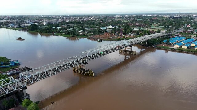 A view from atop the steel truss bridge spanning the Brown River along the urban riverfront with traffic in West Borneo, Indonesia.