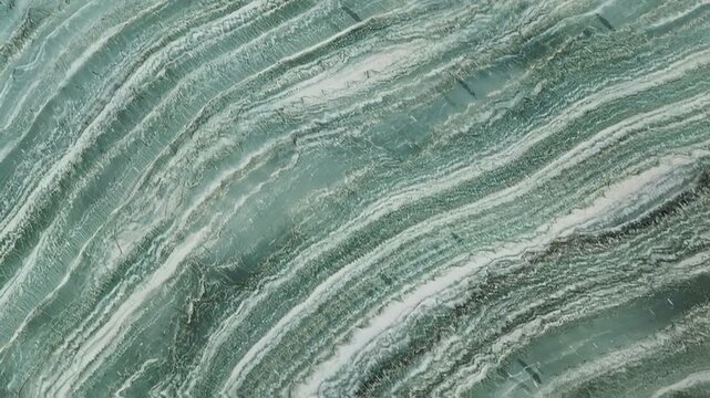 Close-up of rippled green stone texture with white wavy lines. Abstract geological pattern resembling water or waves.