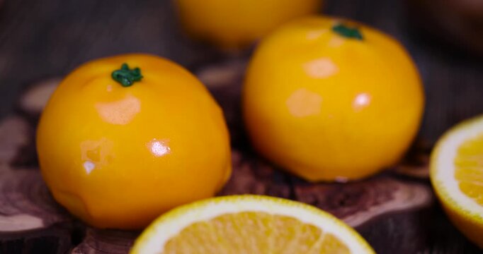 The dessert imitates an orange fruit, an exquisite pastry dessert with a mirror glaze and a tangerine texture on a wooden background with an organic surface and a natural shine in the macro