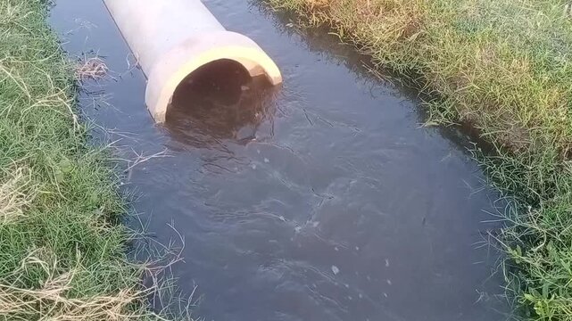 Concrete pipe discharging murky water into a small drainage ditch surrounded by green grassy banks