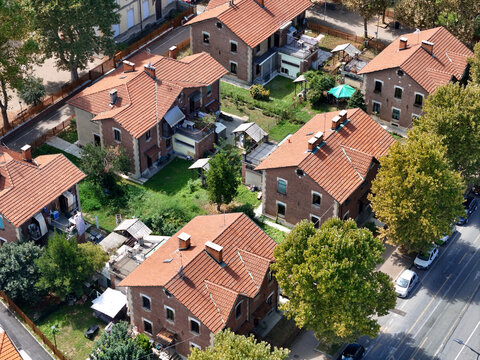 Aerial view of the historic Villaggio Leumann with its characteristic brick houses, red-tiled roofs, and lush green gardens in Collegno, Piemonte, Italy.