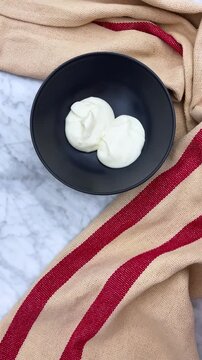 serving greek yogurt from a container into a bowl using a spoon creating a smooth surface.