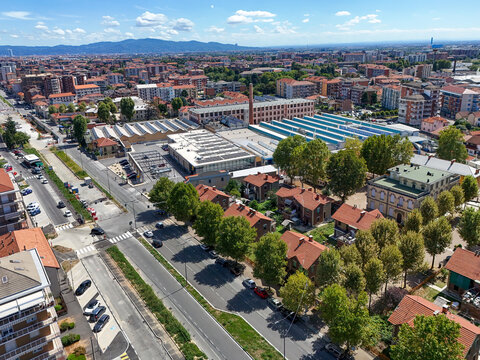 Aerial view of Villaggio Leumann featuring historic industrial buildings, red-roofed houses, and lush green trees along the streets in Collegno, Piemonte, Italy.