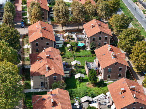 Aerial view of the historic brick houses and red tiled roofs of Villaggio Leumann surrounded by lush green gardens and trees in Collegno, Piemonte, Italy.
