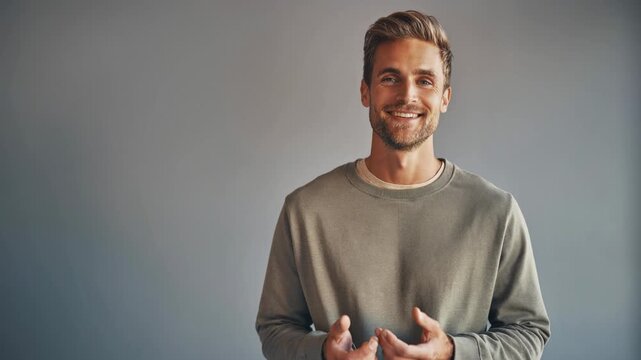Confident young man smiling warmly speaking naturally against plain background