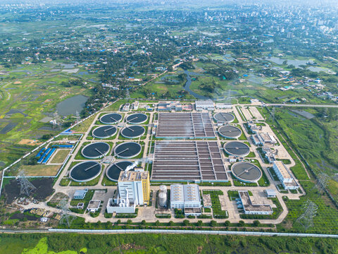 Aerial view of the Sewage Treatment Plant, Dhaka WASA with circular clarifier tanks and rectangular basins surrounded by green fields in Dhaka, Dhaka Division, Bangladesh.
