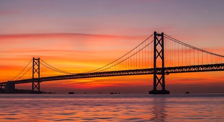 Obraz premium Suspension bridge silhouette against vibrant sunset sky over tranquil water