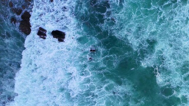 Drone shot of turquoise waves flowing over scattered rocks beneath ocean surface.